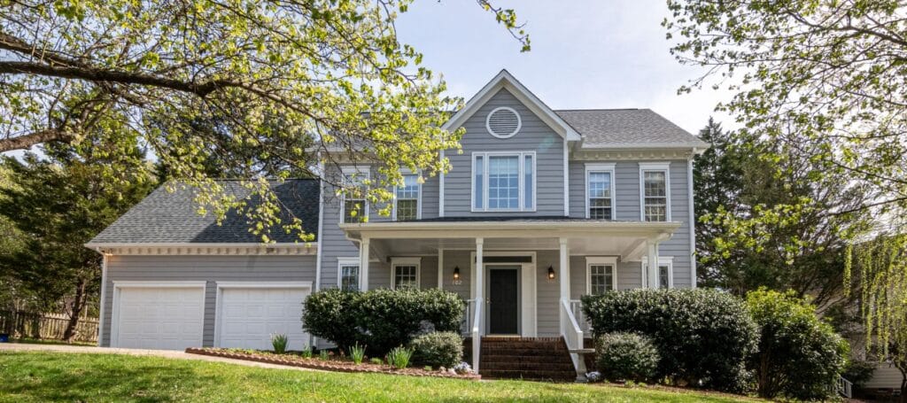 A charming two-story suburban house with a gray exterior surrounded by trees and shrubs